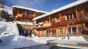 A wooden chalet with a pool, surrounded by snow.