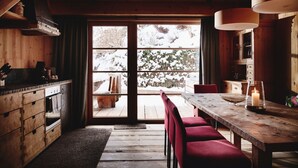L’intérieur d’un chalet en bois, avec une grande fenêtre, une table à manger en bois et des chaises rouges.
