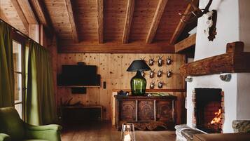 A cozy log cabin interior with a fireplace, wooden walls, a green armchair, and a table with a candle.