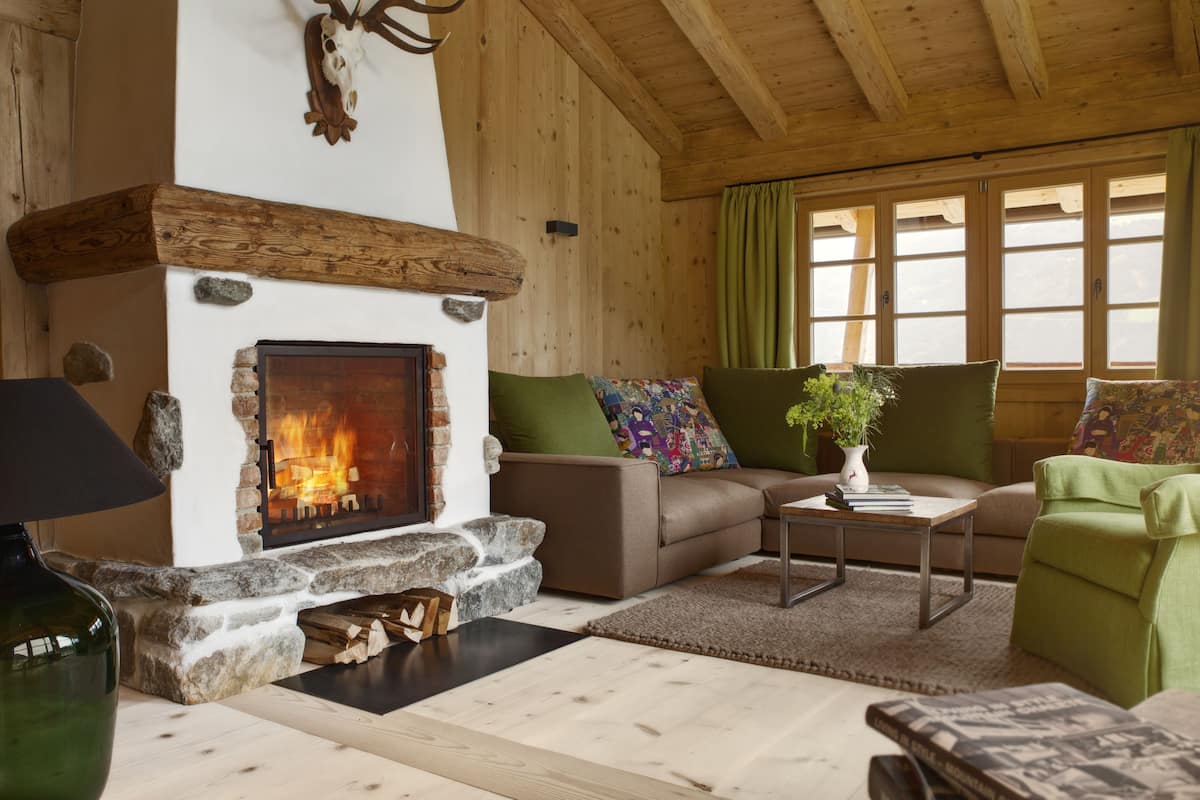 A cozy living room with a stone fireplace, wooden beams, a sofa, and a green armchair.