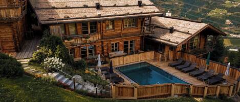 Una cabaña de madera con piscina, rodeada por una terraza y un jardín.