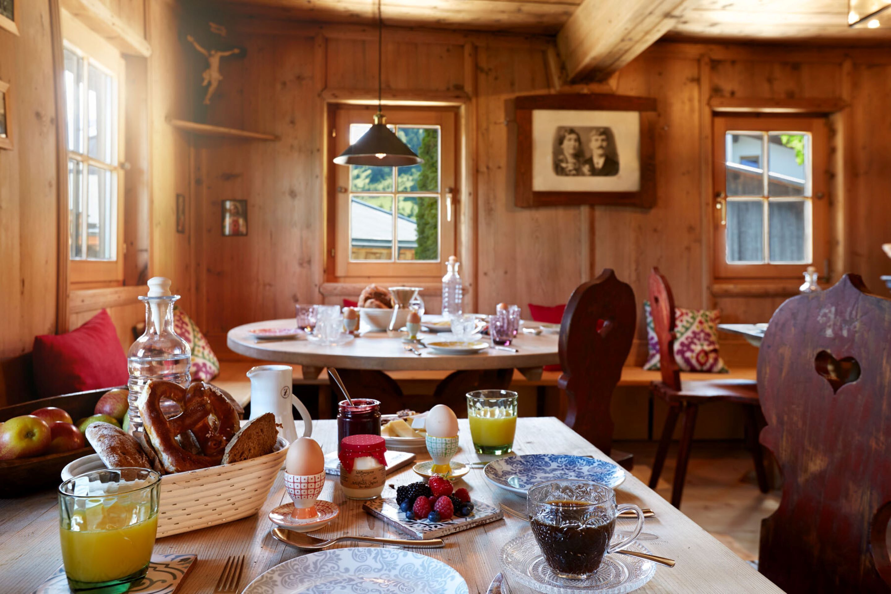 A wooden cabin dining area with a table set for breakfast, including bread, eggs, and fruit.