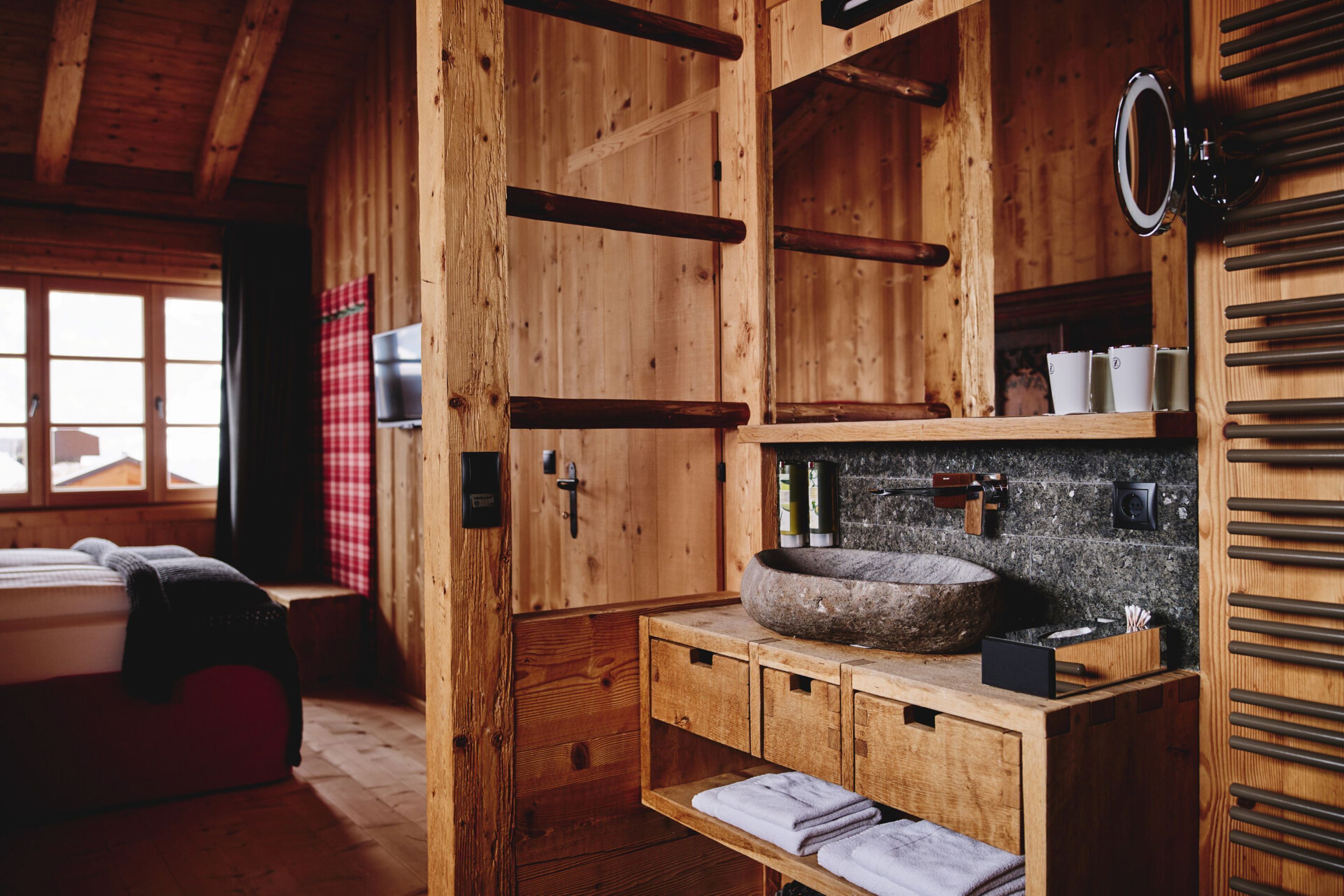 Ein Holzhütten-Interieur mit einem Bett, einem Steinsink und einem Holzregal mit Handtüchern.