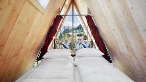 Une chambre avec un plafond en pente en bois, un lit avec une literie blanche et une fenêtre avec des rideaux.