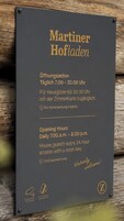 Un letrero con el horario de atención y los servicios de un hotel llamado 'Martiner Hofladen'.