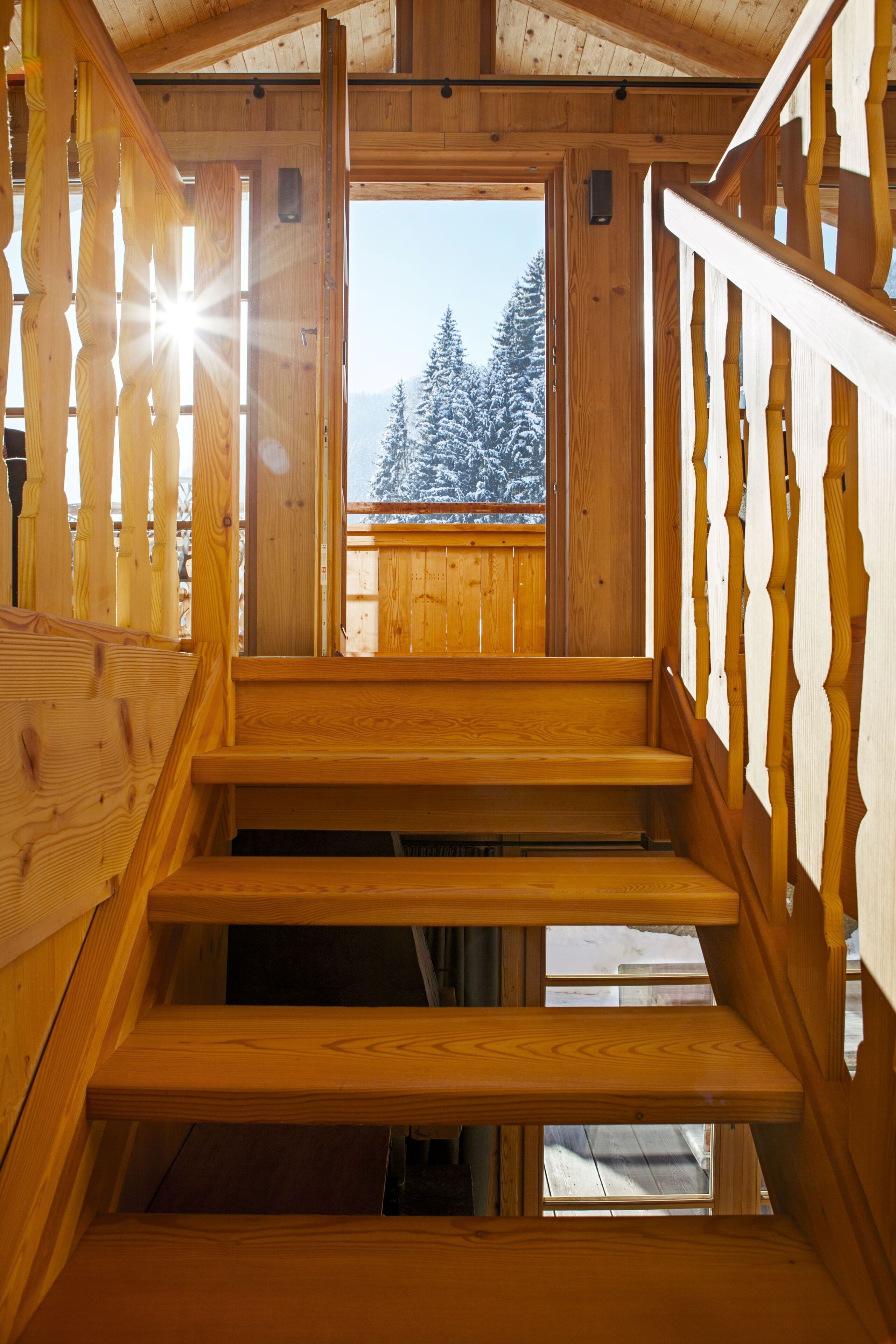 A wooden staircase leading to a balcony with a view of snow-covered trees.