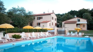 Una piscina con sillas reclinables blancas y sombrillas amarillas, rodeada de edificios y vegetación.