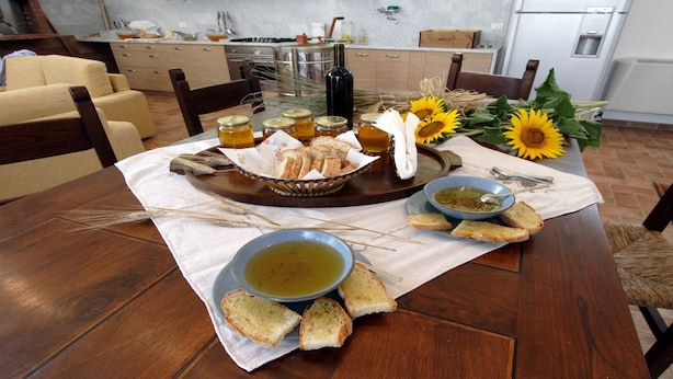 Una mesa de comedor dispuesta con pan, cuencos de sopa y tarros de miel en una cocina.