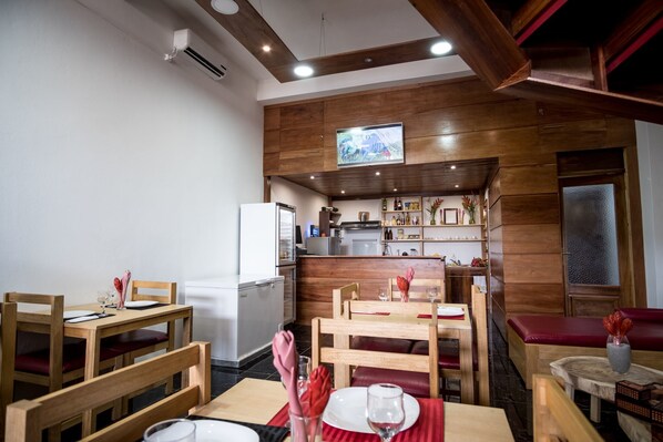A restaurant with wooden furniture, a kitchen area, and a television mounted on the wall.