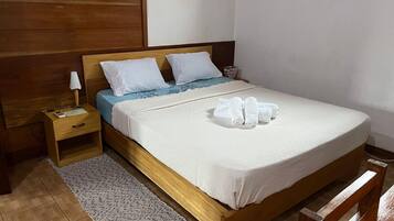 A neatly made bed with white bedding, a blue blanket, and rolled towels on the side.