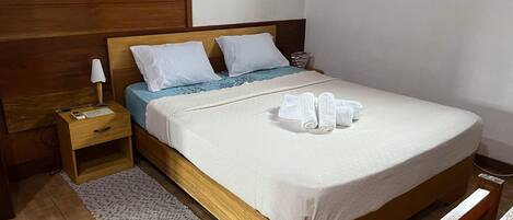A neatly made bed with white bedding, a blue blanket, and rolled towels on the side.
