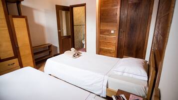 A bedroom with two beds, wooden wardrobes, a bathroom with a toilet, and a small table with items.