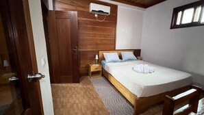 A bedroom with a wooden bed, a nightstand, an air conditioning unit, and a door. - Porcelana Hotel (São Tomé)