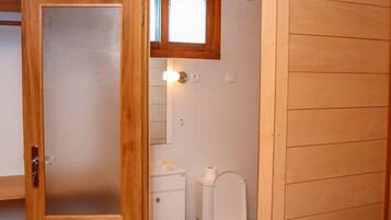 Un bagno piccolo e accogliente, con arredi in legno, porta in vetro satinato, un water bianco e una piccola finestra sopra il lavabo.