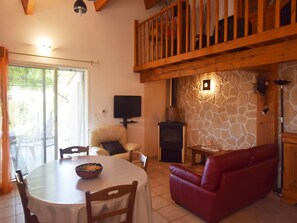 Un salon chaleureux avec une cheminée en pierre, un canapé rouge, une table à manger avec des chaises et un téléviseur fixé au mur.