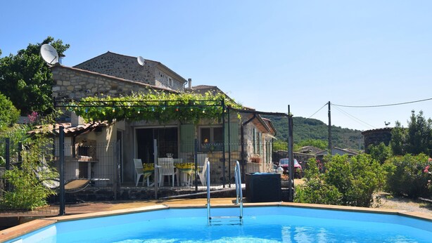 A swimming pool with a wooden deck, a stone building with a satellite dish, and a garden area with chairs and tables. - Relaxing Retreat in Saint-Pons (Saint Pons)