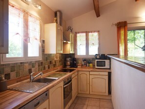 Une cuisine de taille réduite, équipée d’un évier, d’une cuisinière, d’un four à micro-ondes et d’une fenêtre avec des rideaux.