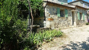 A stone building with green shutters, a gravel path, and surrounding vegetation. - Relaxing Retreat in Saint-Pons (Saint Pons)