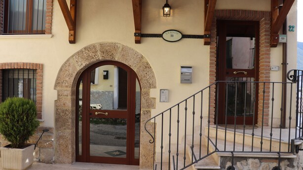 Une entrée d’immeuble avec un arc en pierre, une porte en bois et un escalier en métal.