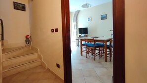 Un escalier menant à une salle à manger équipée d’une table et de chaises, d’un téléviseur et d’une horloge murale.