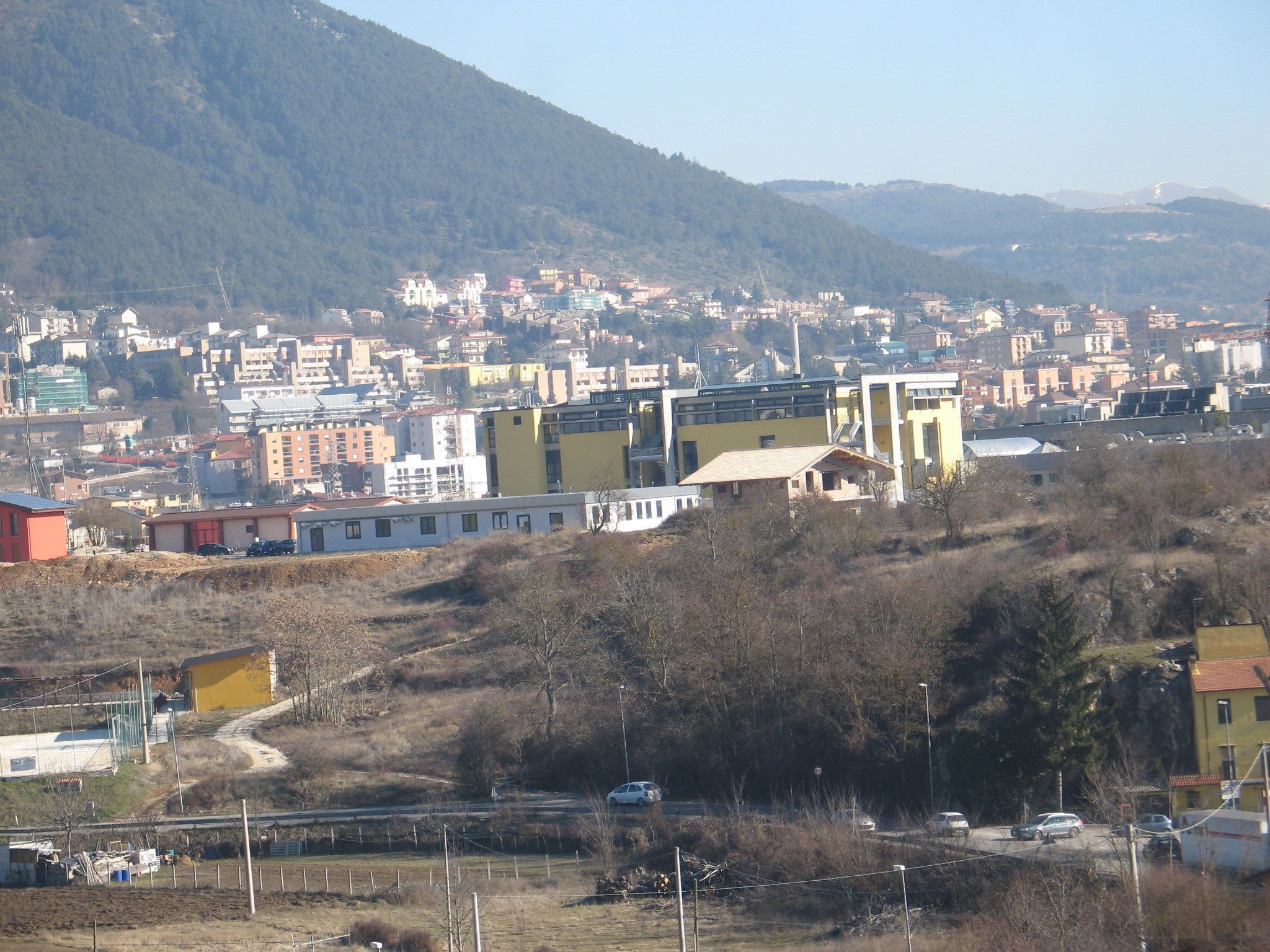 Uma cidade com edifícios, uma estrada e um cenário montanhoso.