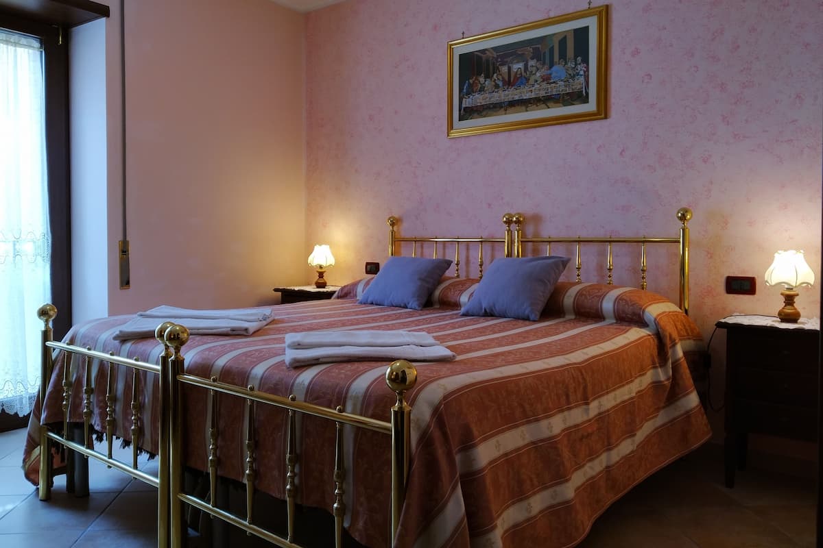 A hotel room with a bed, two bedside tables, a painting on the wall, and a window with curtains.