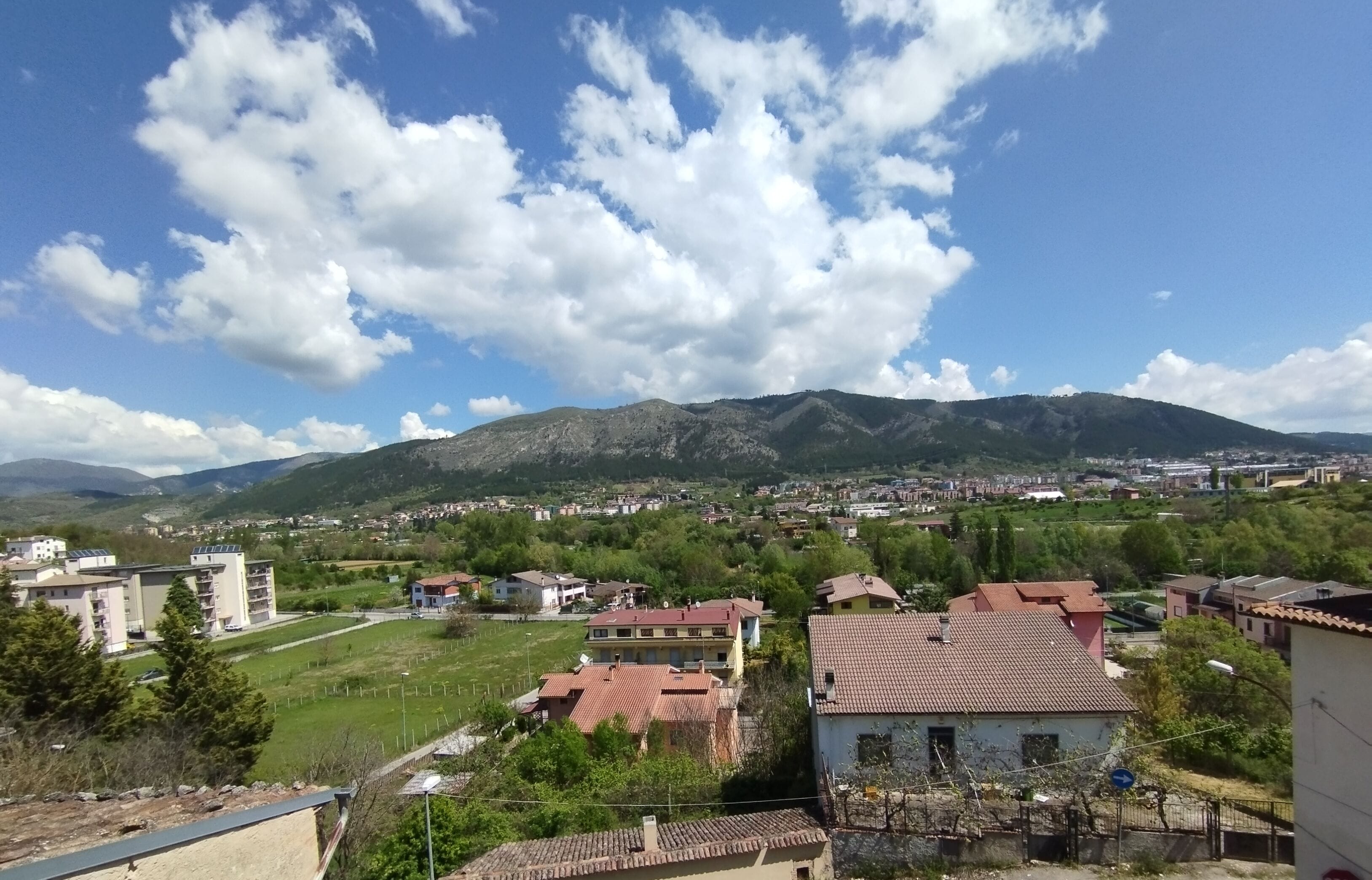 Zona residencial com casas, um campo verde e montanhas ao fundo.