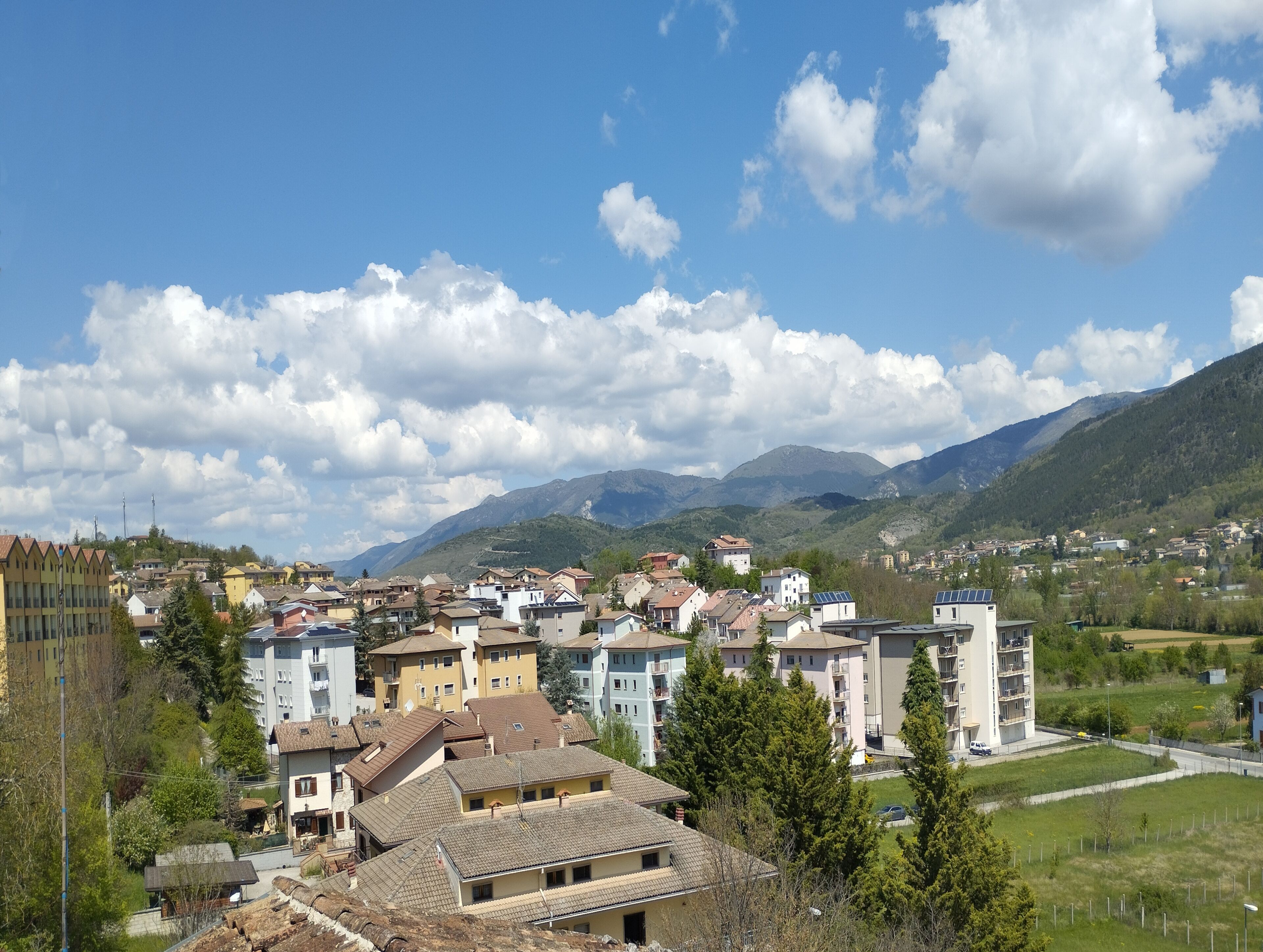 Un quartier résidentiel où se côtoient différents types de bâtiments, notamment des immeubles d’habitation à plusieurs étages et des maisons unifamiliales, le tout sur fond de montagnes et sous un ciel dégagé.