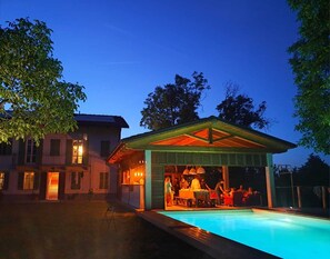 A poolside area with a covered seating area and a building with open windows.