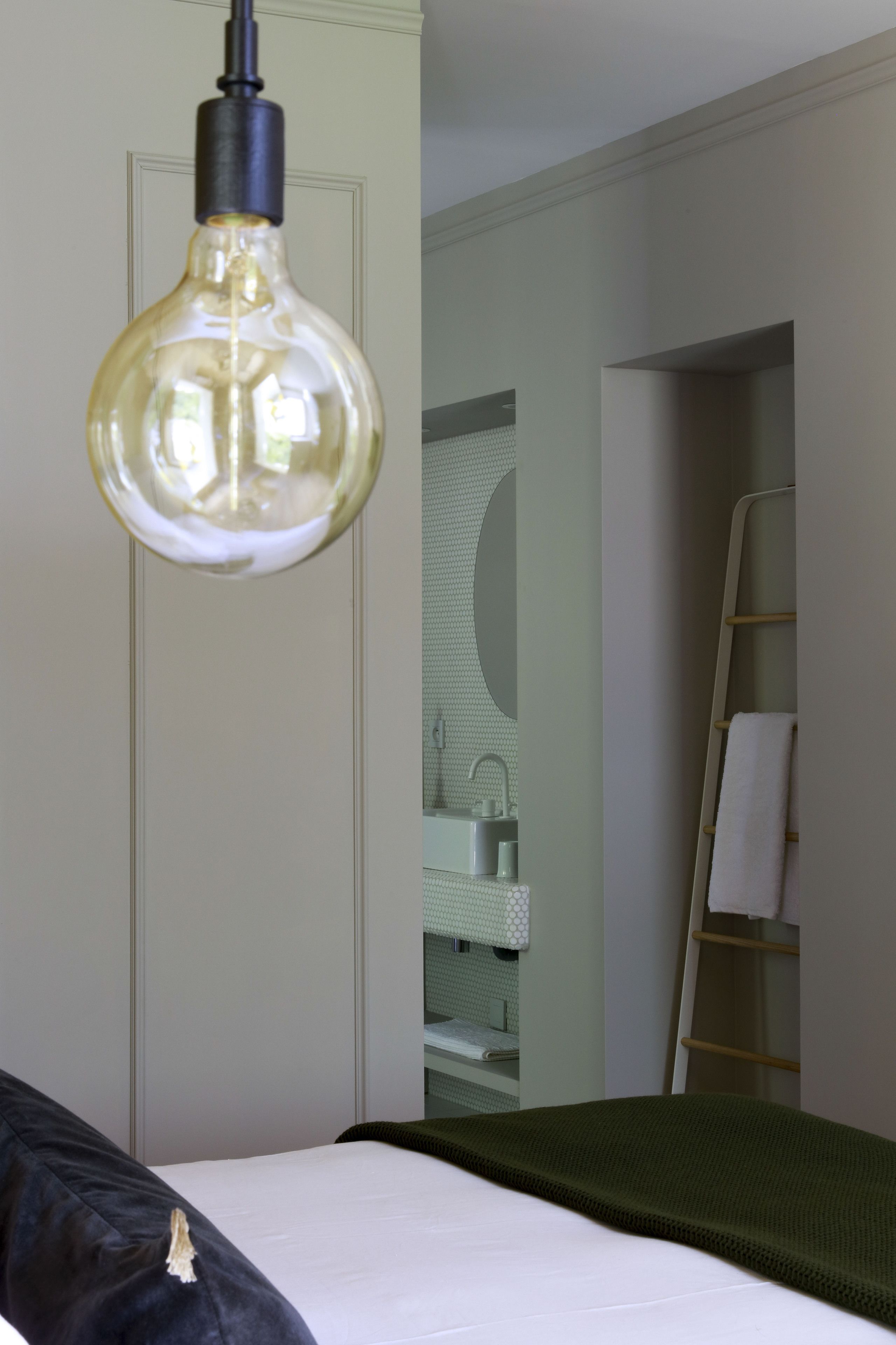 Habitación de hotel con cama, lámpara colgante, baño con lavamanos y espejo, y toallero.