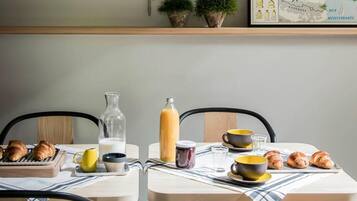 A dining area with a table set for breakfast, including croissants, a bottle of milk, and a juice pitcher. There are two chairs and a map on the wall above the table.