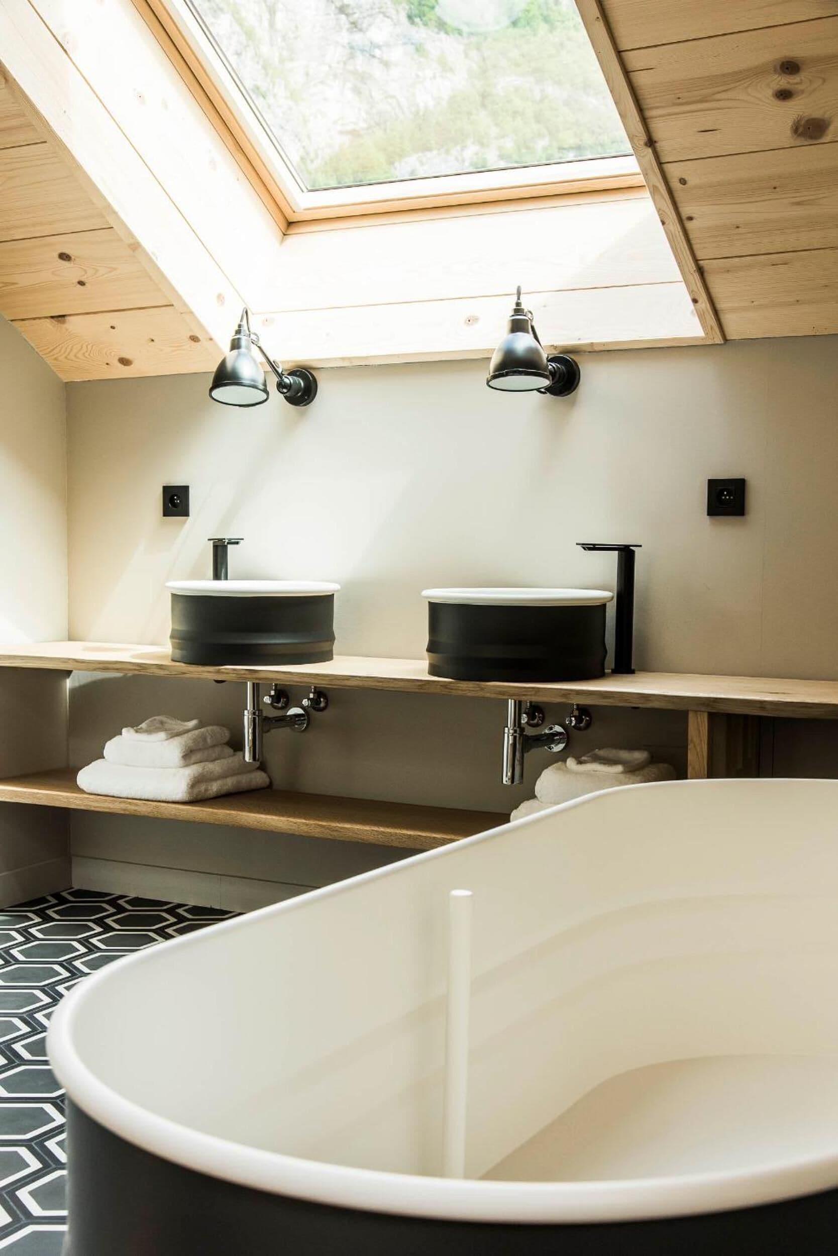 A modern bathroom with a skylight, two sinks, a bathtub, and wooden shelves.