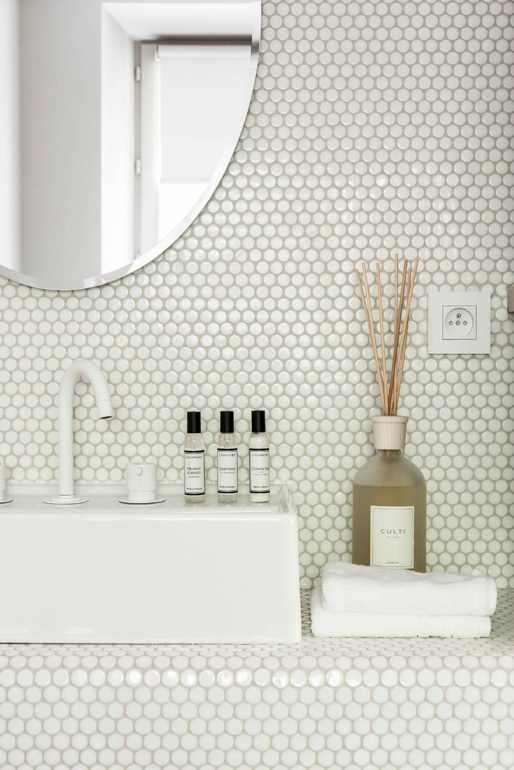 A bathroom with a white sink, three bottles of skincare products, a bottle of essential oil, and a white towel on the counter.