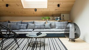 Une chambre de style loft moderne avec un plafond en pente, une fenêtre intégrée, un grand canapé, une table ronde et un fauteuil décoratif.