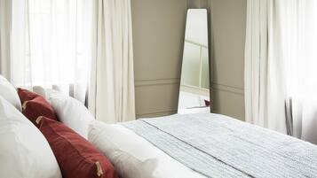 A neatly made bed with white and red pillows, a light blue blanket, and a large mirror on the wall.