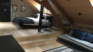 A loft bedroom with a sloped ceiling, a bed, a sofa, a desk, and a wardrobe.