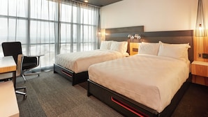 A hotel room with two beds, a desk, a chair, and a large window with sheer curtains. - Alt Hotel Calgary East Village (Calgary)