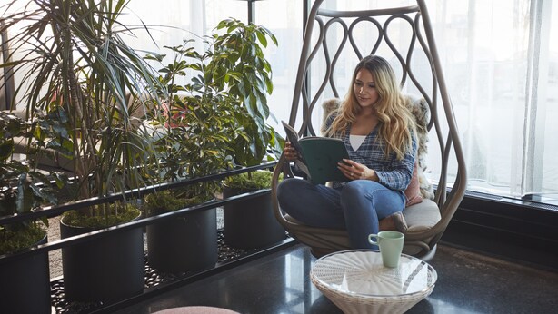 A person sitting in a hanging chair by a window with potted plants. - Alt Hotel Calgary East Village (Calgary)