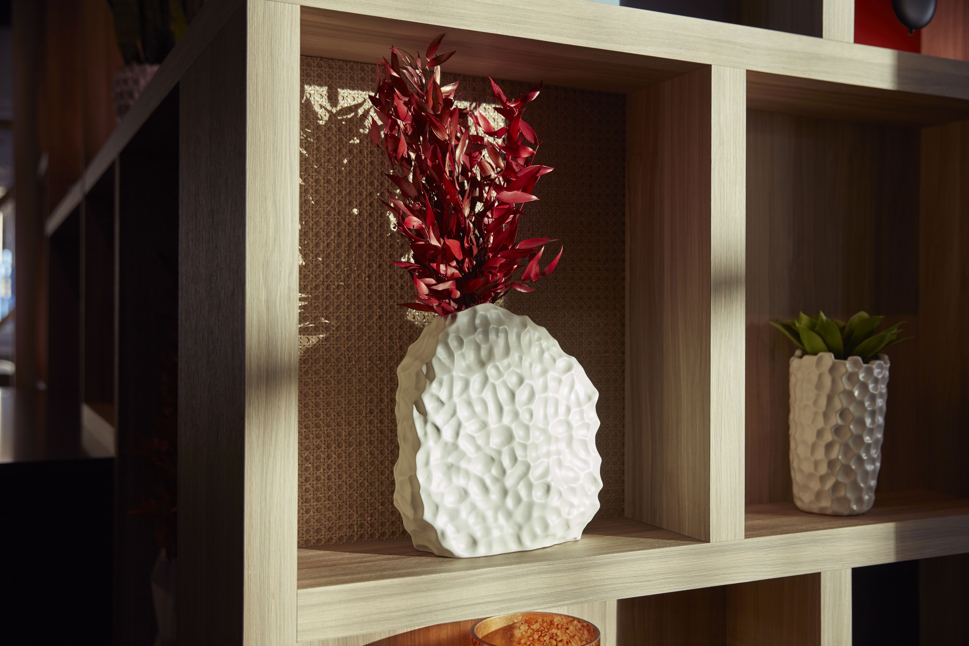 Una estantería de madera con dos jarrones decorativos, uno con follaje rojo y el otro con follaje verde.