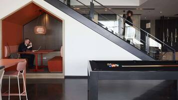 Un interior moderno con una escalera, mesa de billar y zona de estar con una persona usando una computadora portátil.