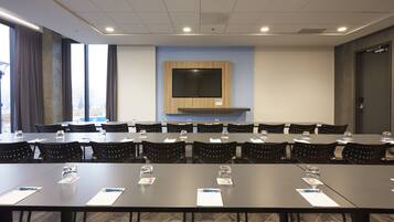 A conference room with multiple tables and chairs, a mounted television, and a large window with curtains.