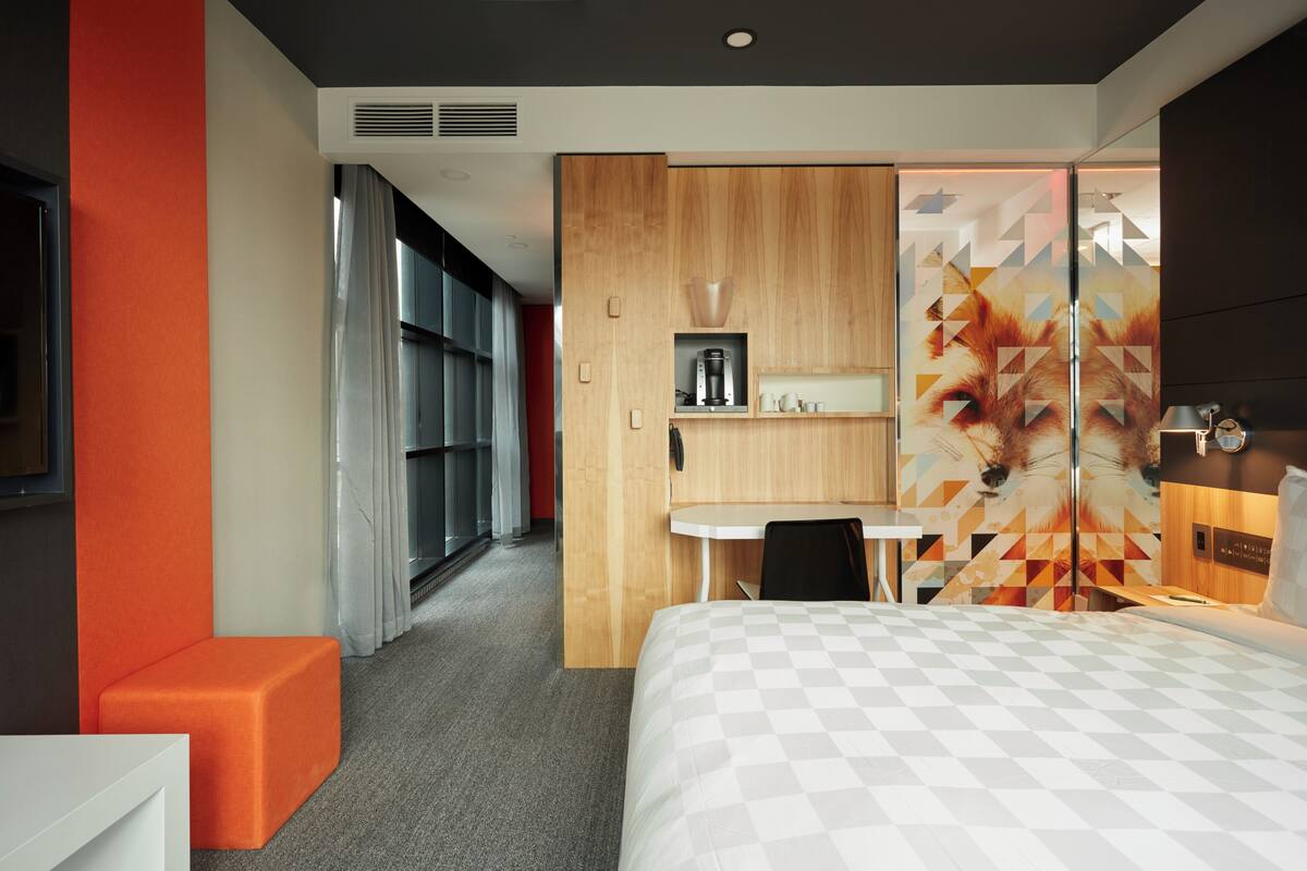 A modern hotel room with a bed, a desk, and a seating area.