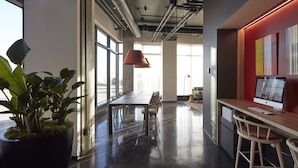 A modern office space with a large desk, chairs, a potted plant, and a computer monitor. - Alt Hotel Calgary East Village (Calgary)