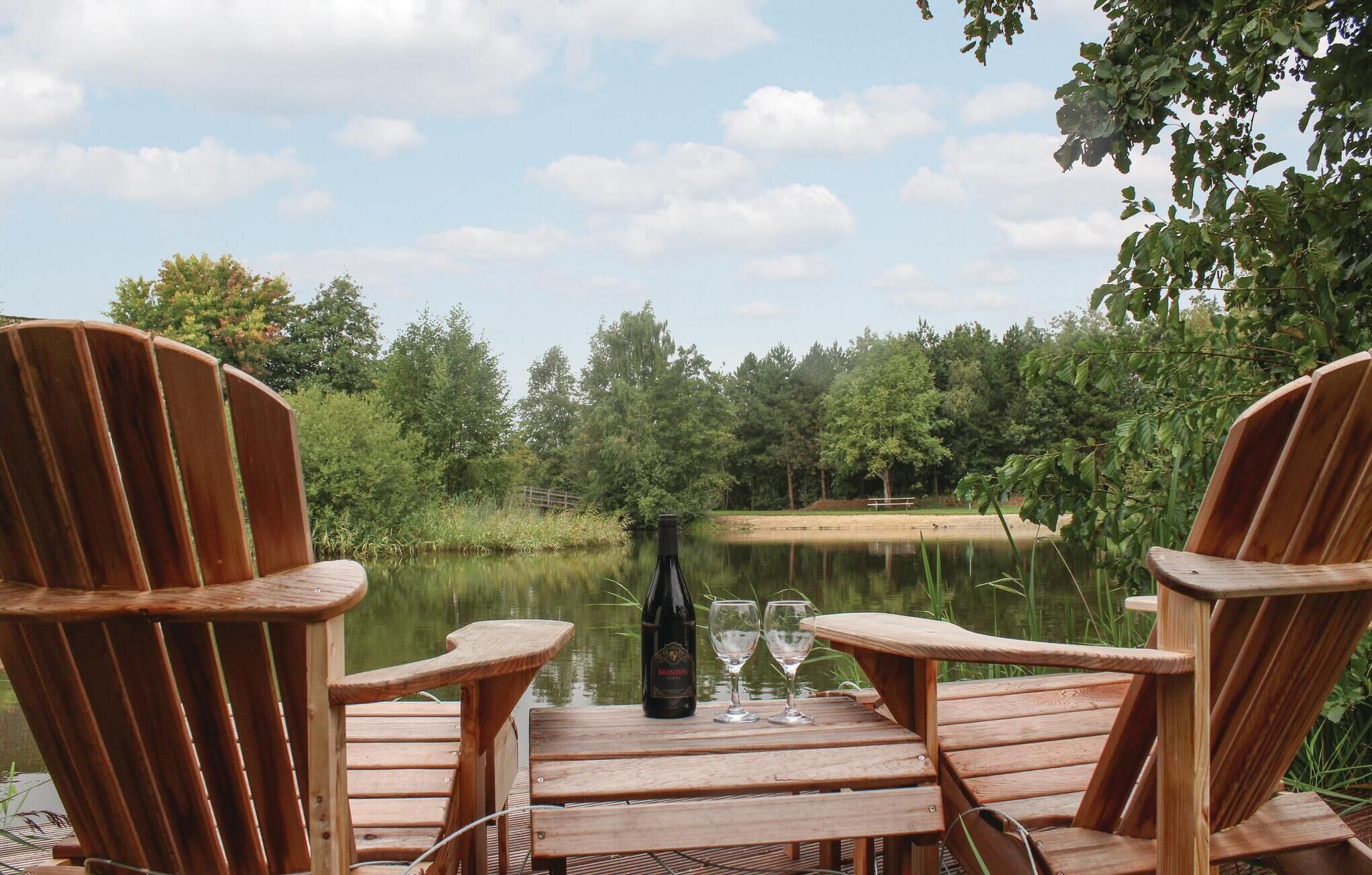 Eine Holzterrasse mit Adirondack-Stühlen, die auf einen ruhigen See blicken, umgeben von Bäumen.