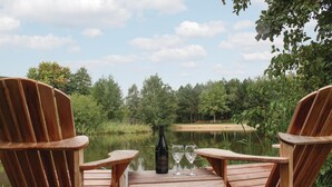En træterrasse med Adirondack-stole vendt mod en rolig sø, omgivet af træer.