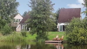 En ejendom ved søen med en træbrygge, et overdækket siddeområde og et hus med rødt tegltag.