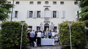 A group of people gathered around a table with a white tablecloth in front of a building with white walls and shutters. - Villa Cigolotti (Vivaro)