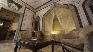 A room with ornate ceiling and wall decorations, a bed with white curtains, and a patterned sofa. - Villa Cigolotti (Vivaro)