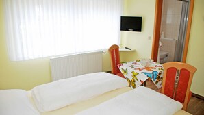 Een kamer met twee bedden, een televisie aan de muur, een douche en een raam met zonwering.