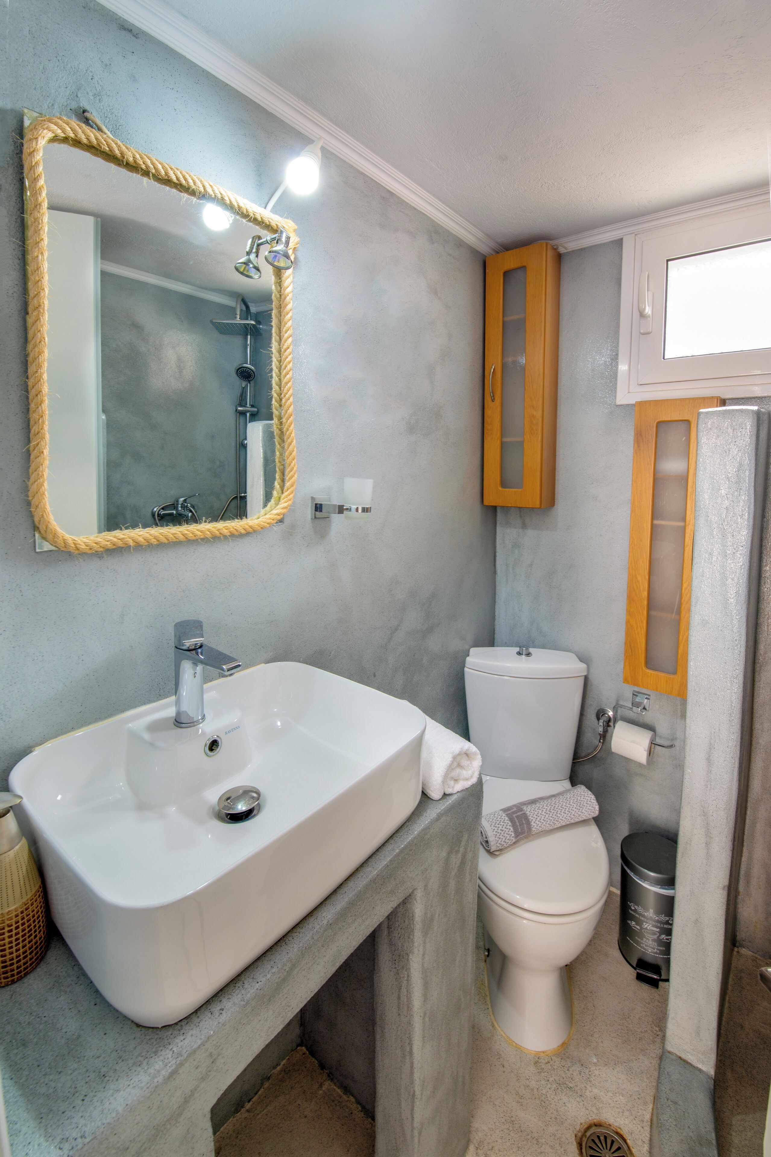 A bathroom with a white sink, a toilet, and a mirror with a rope frame.